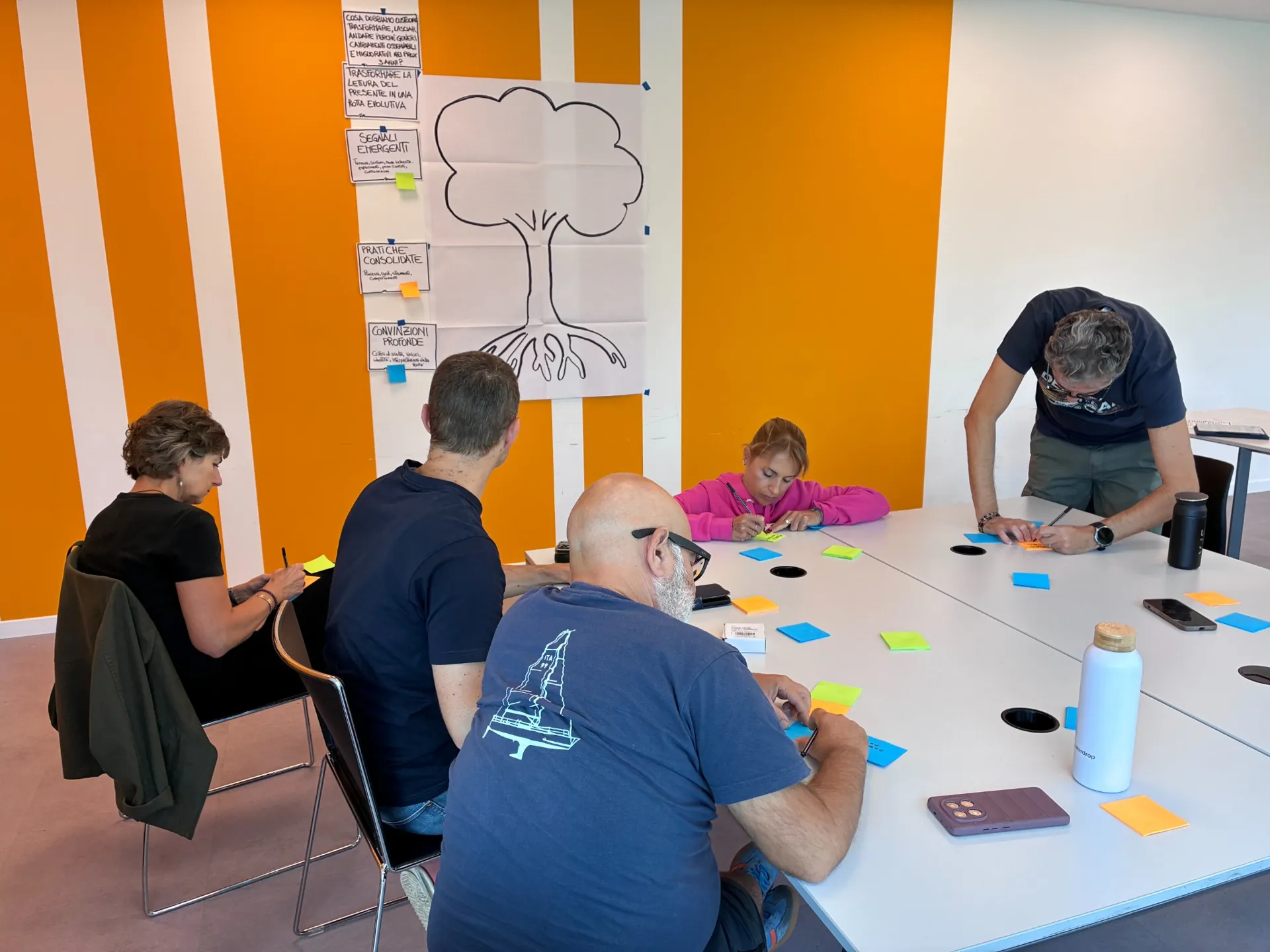 I partecipanti annotano le proprie riflessioni su post-it davanti all’albero delle ipotesi durante il laboratorio Radici e Rotte.