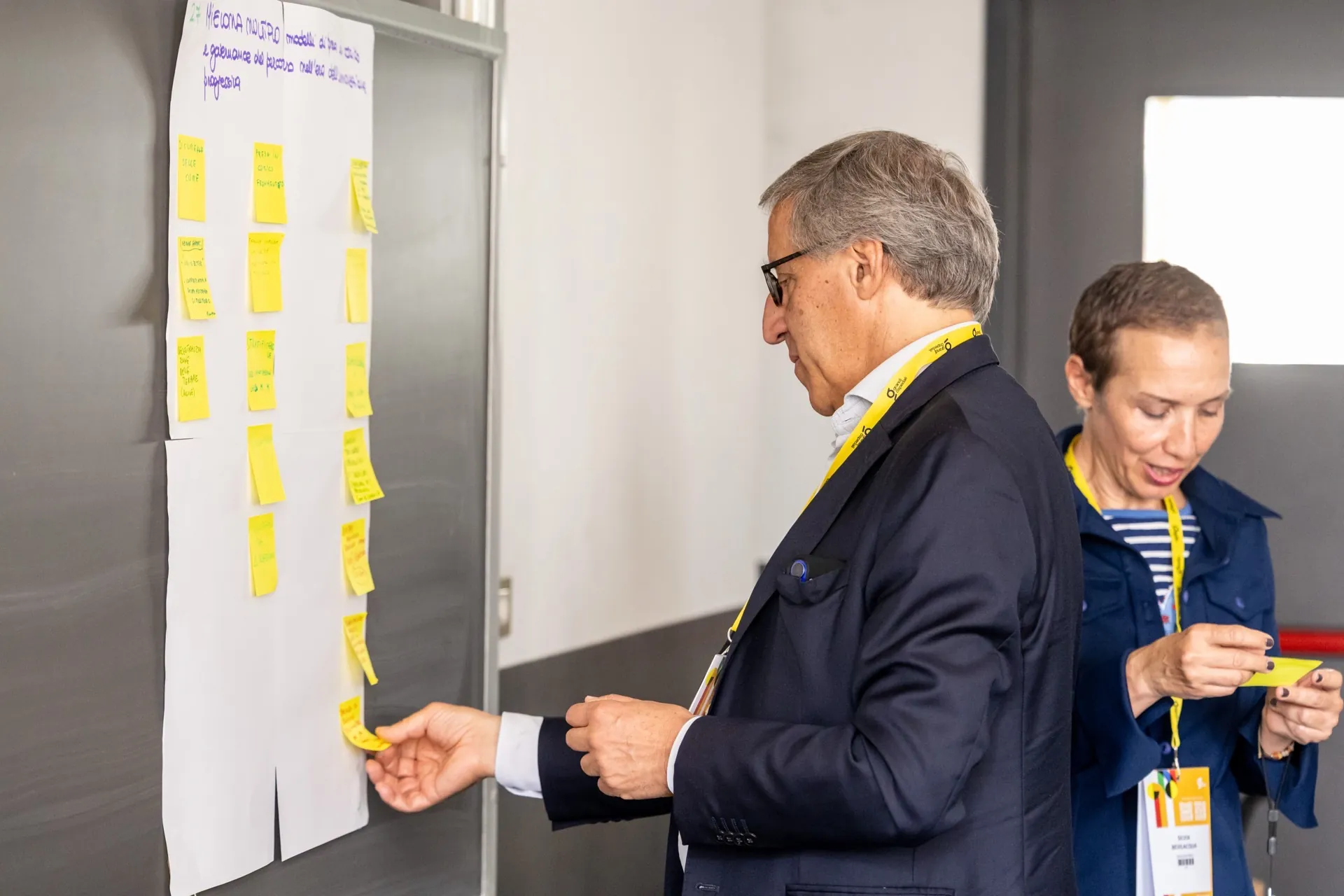 Due partecipanti organizzano i contributi su post-it per individuare priorità condivise in ambito sanitario.